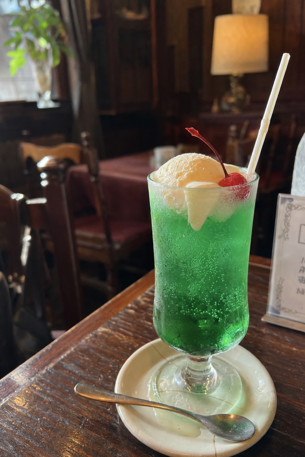 古い喫茶店のテーブルに置かれた、アイスクリームとさくらんぼの乗ったメロンクリームソーダ。